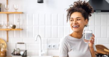 Image of a woman in a kitchen drinking a glass of water.