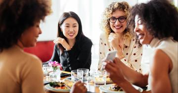 Women together at a table looking at a phone and talking about nutrition and fertility