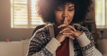 Woman sitting with her eyes closed and hands clasped in front of her face, in the midst of her TTC affirmations practice.