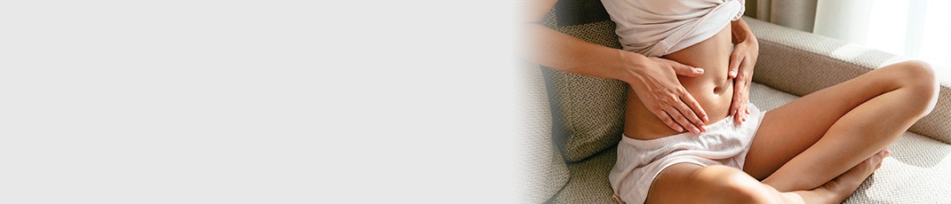 Woman sitting crossed legged on the floor with her midriff exposed holding her hands over her abdomen